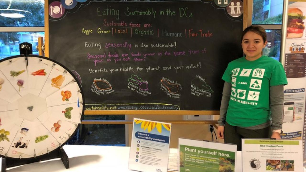 UC Davis Dining Sustainability Intern tabling on the topic of sustainable food options, highlighting sustainable food menu icon definitions, such as Aggie Grown and Local. Photo Credit Skylar Johnson, Student Housing and Dining Services.