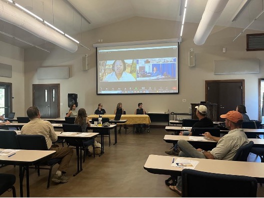 People in a classroom are listening to a speaker on a screen