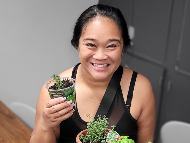 Smiling woman holds potted plant and displays a potted herb garden.