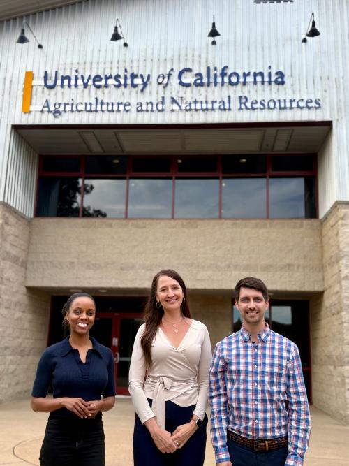 Two women and a man standing side by side outside a building.
